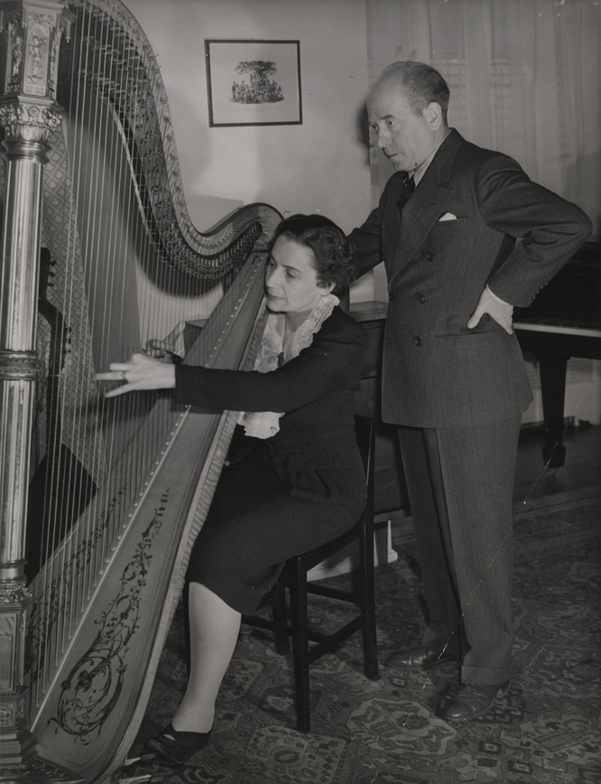 Photograph of Steffy Goldner seated playing harp with Eugene Ormandy standing behind her.